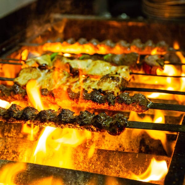 Mediterranean kebabs, including koobideh and chicken, grilling over open flames at Faz Restaurants & Catering.