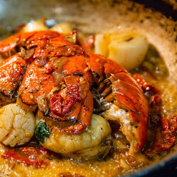 Close-up of a Faz Restaurants & Catering dish with lobster, scallops, and sun-dried tomatoes in a rich sauce.
