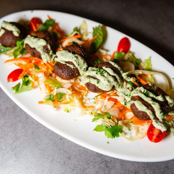 Mediterranean falafel with green sauce, shredded carrots, cabbage, and cherry tomatoes on a white plate.