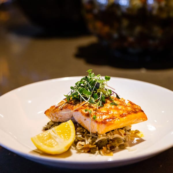 Grilled salmon fillet with microgreens, rice, and a lemon wedge on a white plate.