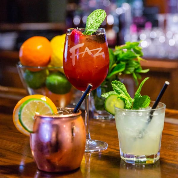 Three Faz cocktails on a bar, including a red Faz-branded drink, a Moscow Mule, and a clear drink.
