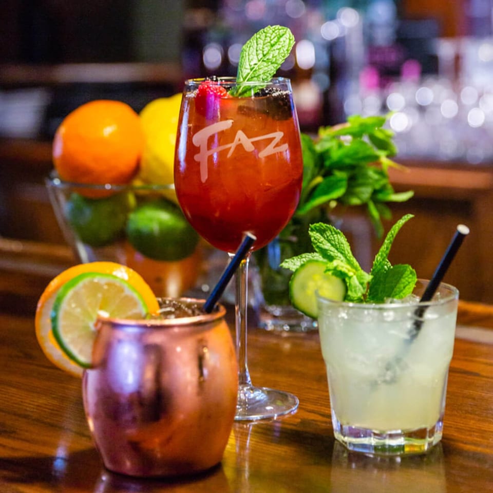 Three Faz cocktails on a bar, including a red Faz-branded drink, a Moscow Mule, and a clear drink.