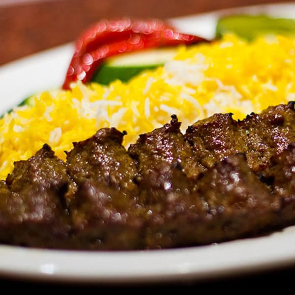 Mediterranean koobideh kebab with saffron rice, a red pepper, and green garnish on a white plate.