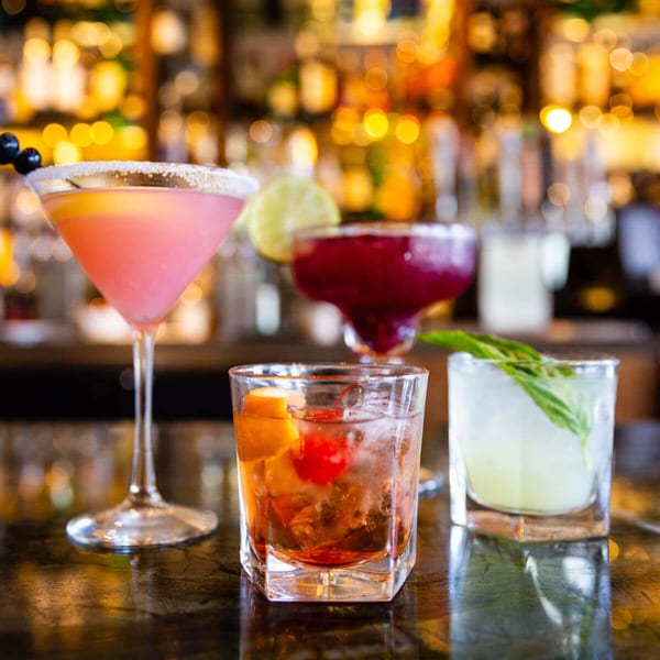 Four colorful cocktails, including a pink martini and an old fashioned, on a bar counter.