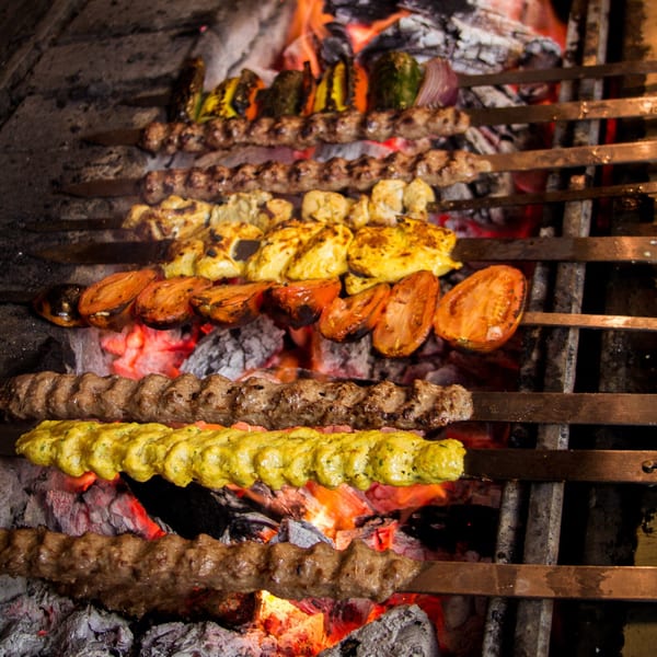 Mediterranean kebabs, including meat, chicken, and vegetables, grilling over hot coals.