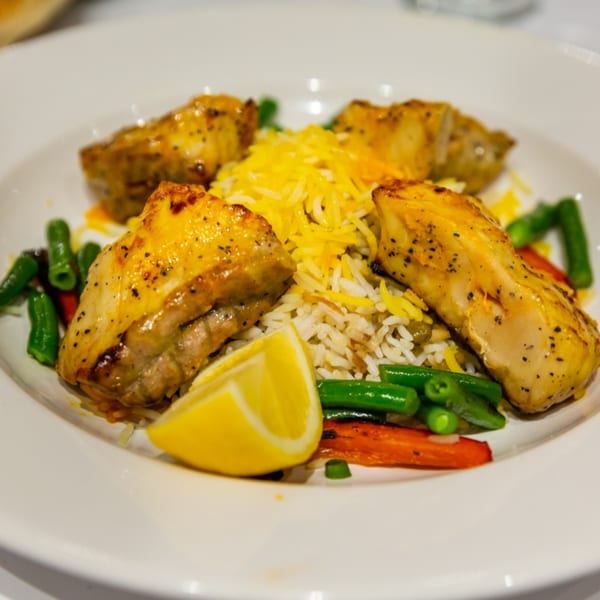Mediterranean chicken and rice dish with green beans, carrots, and a lemon wedge.