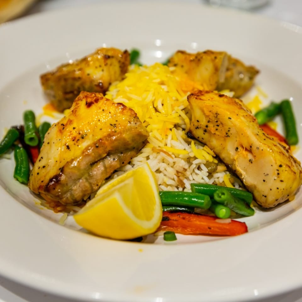 Mediterranean chicken and rice dish with green beans, carrots, and a lemon wedge.