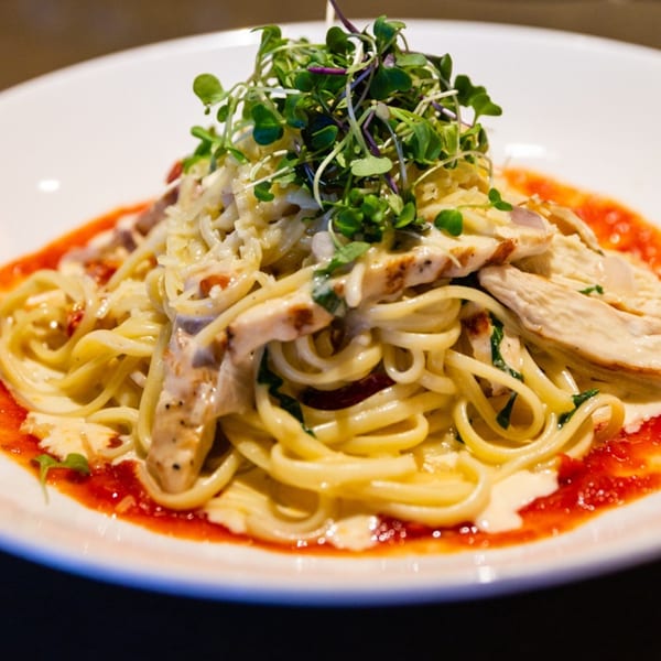 Linguine pasta with grilled chicken, creamy sauce, red sauce, and microgreens on a white plate.