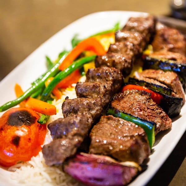 Two skewers of grilled Mediterranean beef and vegetable kebabs with rice and roasted vegetables.