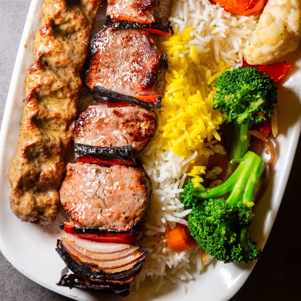Mediterranean platter with two skewers of grilled meat, yellow and white rice, and steamed broccoli.
